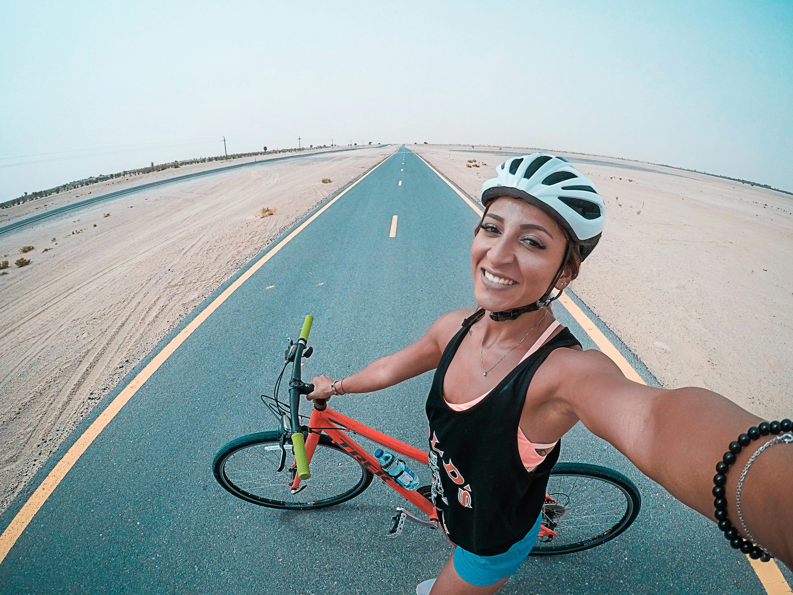 Home Young woman cycling on a desert road in Dubai, enjoying fitness and leisure.